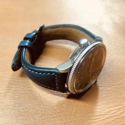 Relógio com bracelete de pele preta e caixa metálica prateada sobre superfície de couro castanho