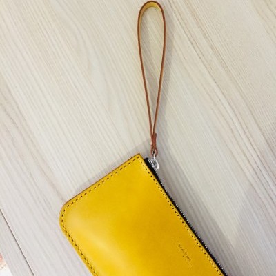 Carteira amarela de pele com asa castanha num fundo de madeira clara