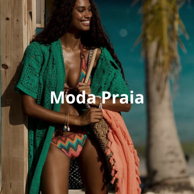 Mulher com fato de banho colorido, cardigan verde e toalha cor de coral na praia.