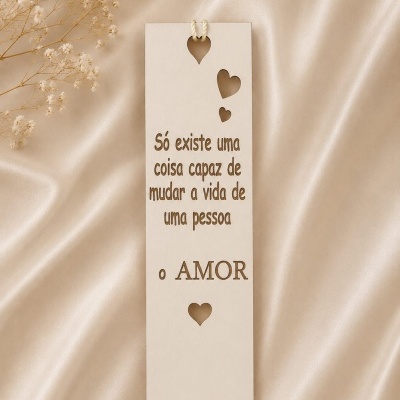Marcador de livro de madeira clara com frase sobre o amor e recortes em forma de corações sobre tecido bege acetinado.