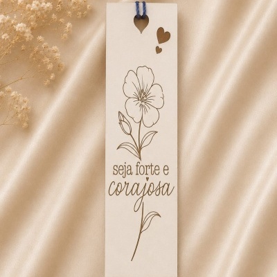 Marcador de livros creme com desenho de flor e corações, texto gravado seja forte e corajosa sobre tecido acetinado.