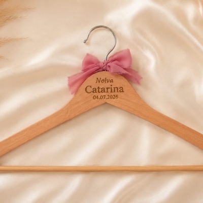 Cabide de madeira personalizado com laço rosa sobre tecido de cetim bege e plantas secas