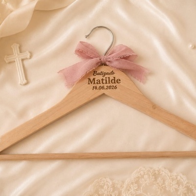 Cabide de madeira com laço rosa e gravação para batizado sobre tecido acetinado