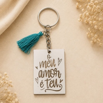 Porta-chaves branco com gravação e tassel azul fotografado sobre fundo bege com flores secas