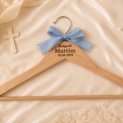 Cabide de madeira com fita azul e texto Batizado Martim 14.06.2026 em tecido creme com decoração religiosa