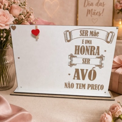 Placa decorativa branca com texto sobre ser avó, com coração vermelho, perto de flores e presentes rosa.