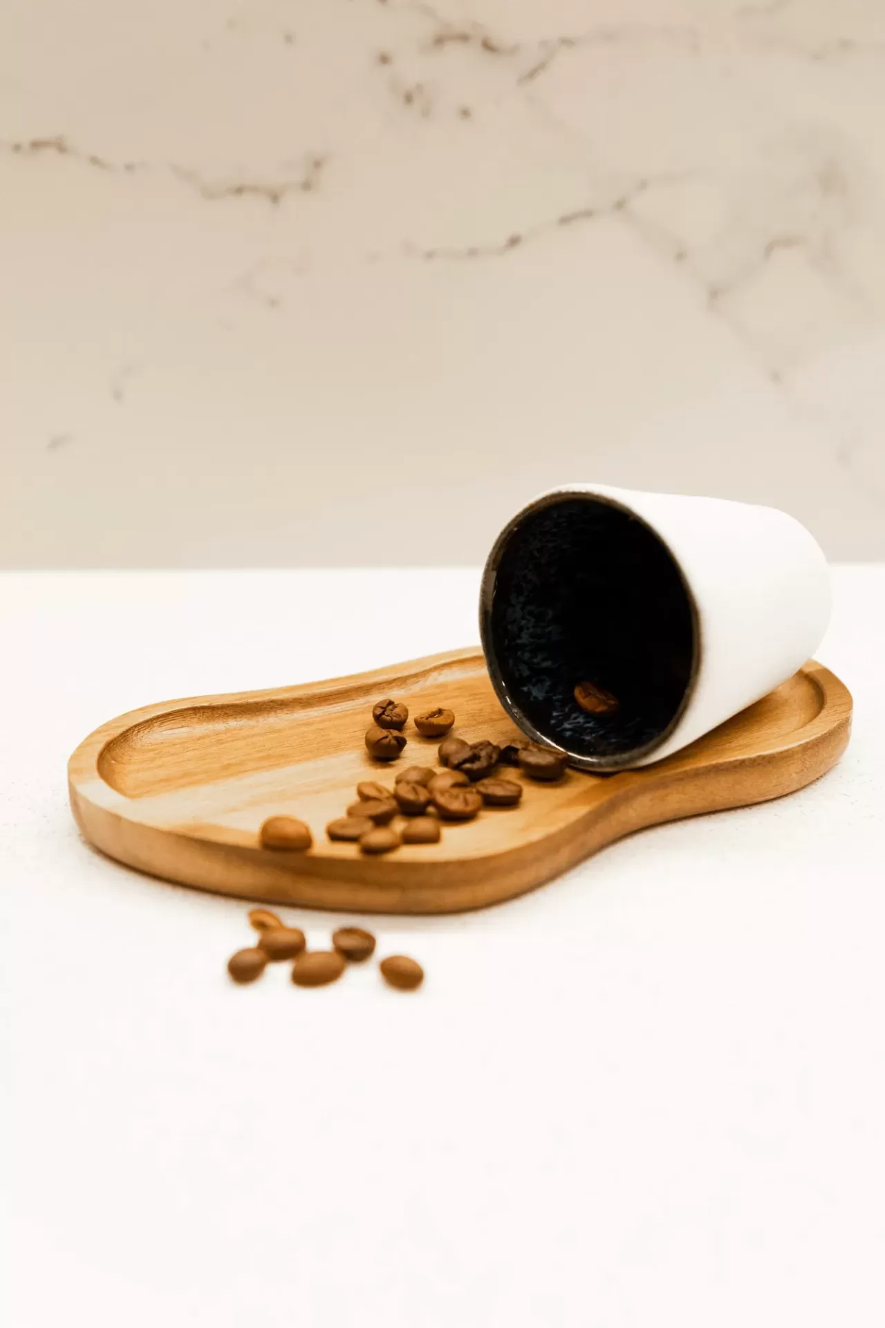 Copo de cerâmica branco com interior preto em bandeja de madeira com grãos de café.