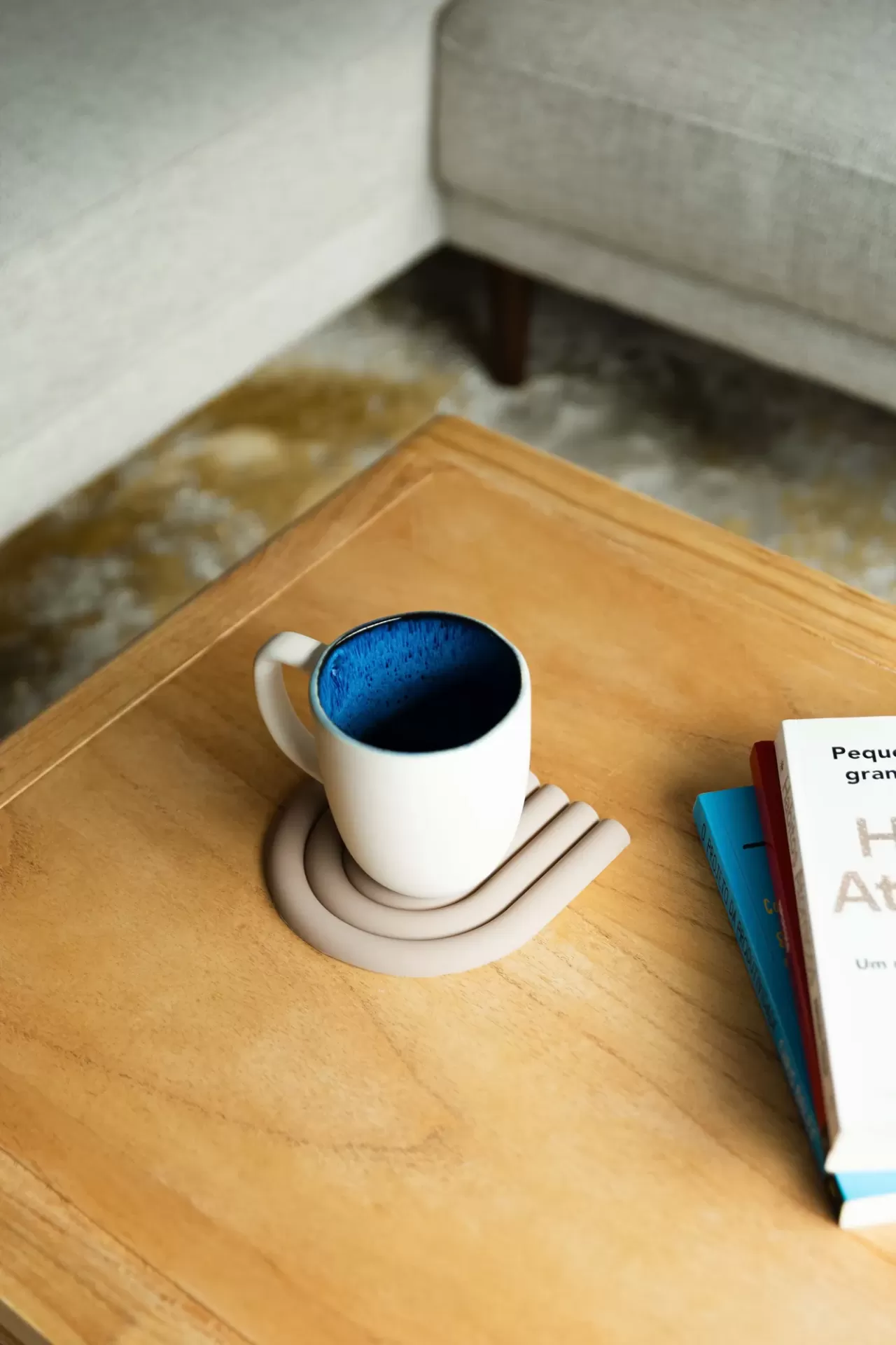 Caneca branca com interior azul numa mesa de madeira perto de livros e sofá