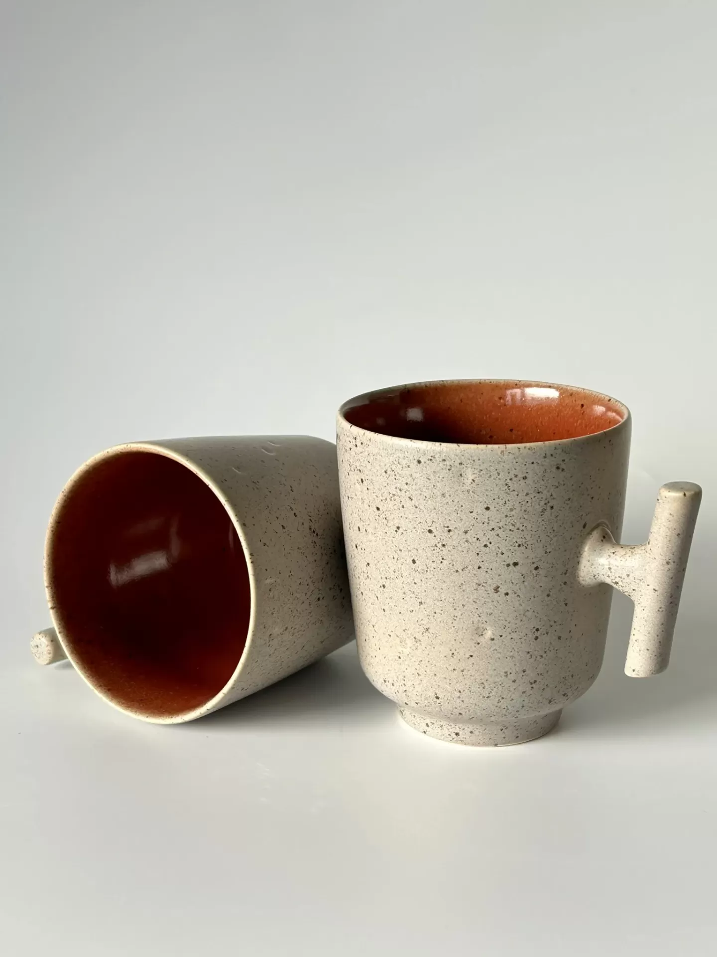 Duas canecas de cerâmica bege com interior vermelho castanho e pegas cilíndricas horizontais