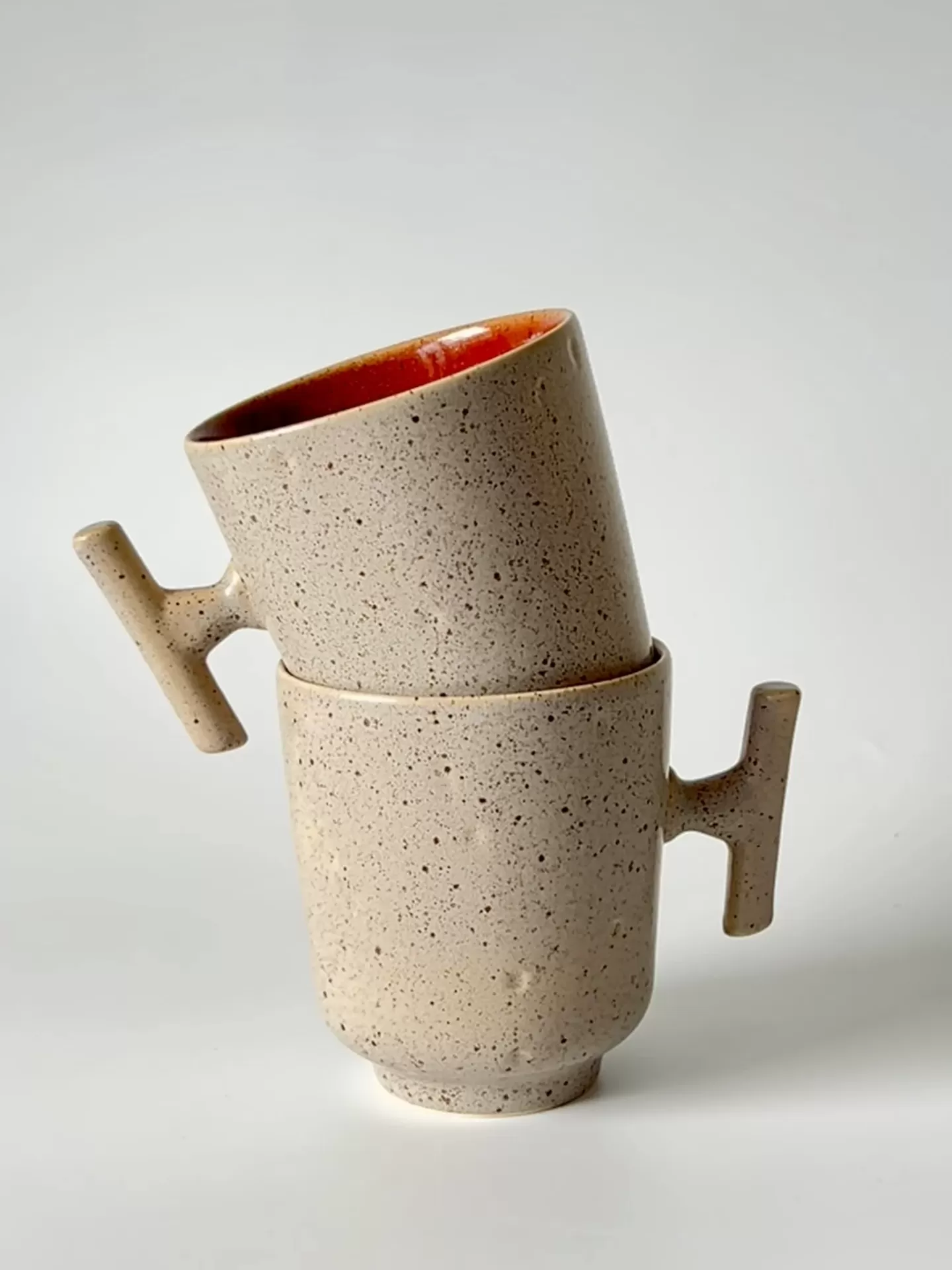 Duas chávenas de cerâmica bege com interior laranja e pega em barra