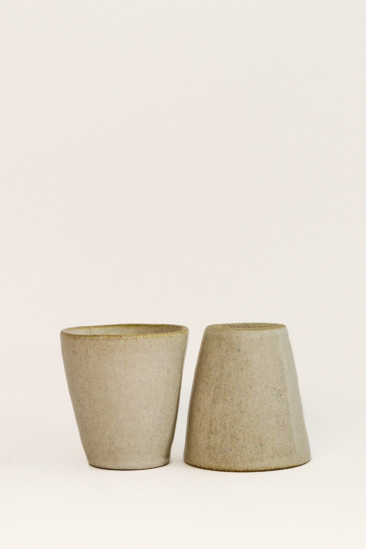 Dois copos de cerâmica bege com textura rugosa em fundo branco.