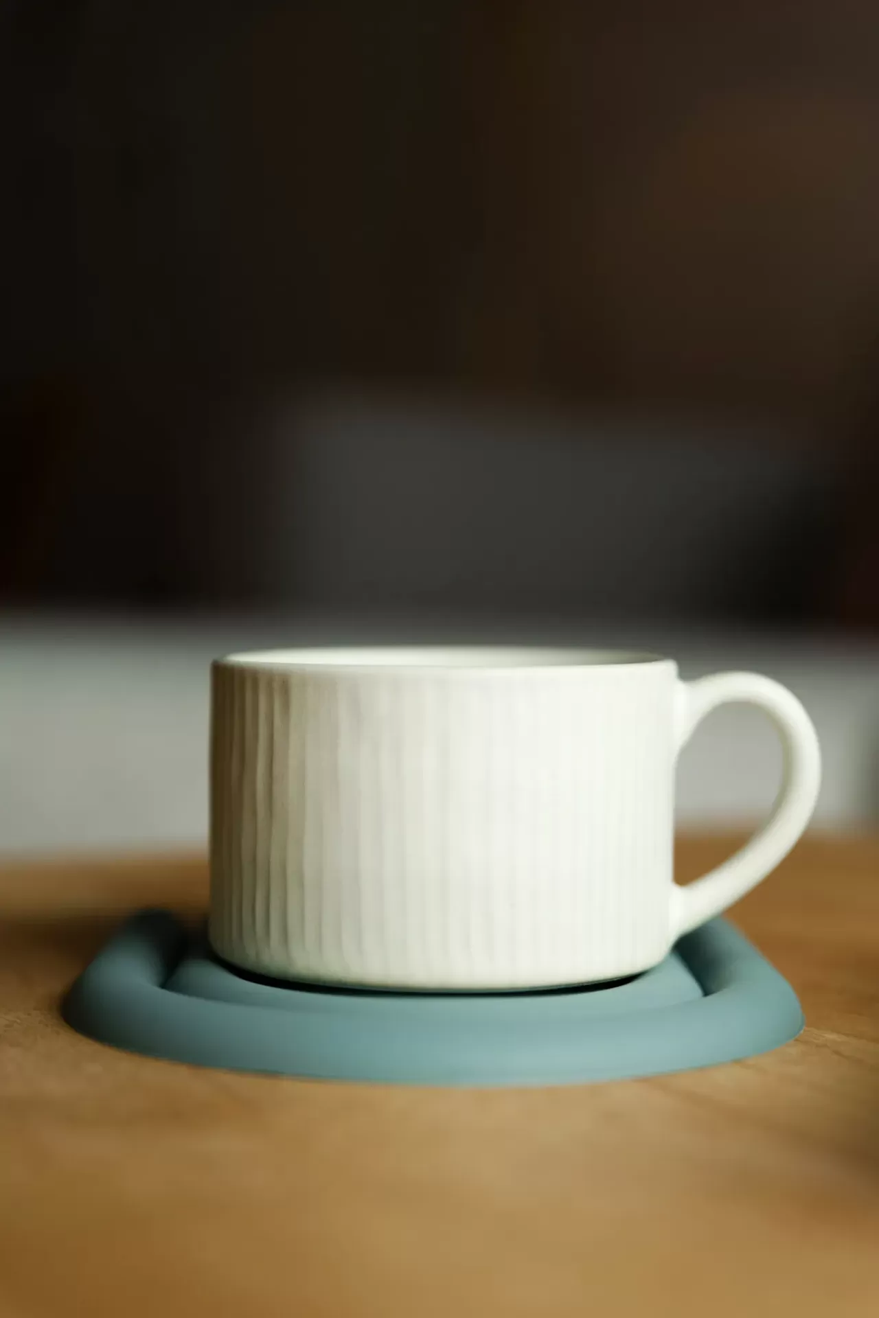 Caneca branca em cerâmica com padrão de relevos verticais sobre suporte azul numa mesa de madeira.