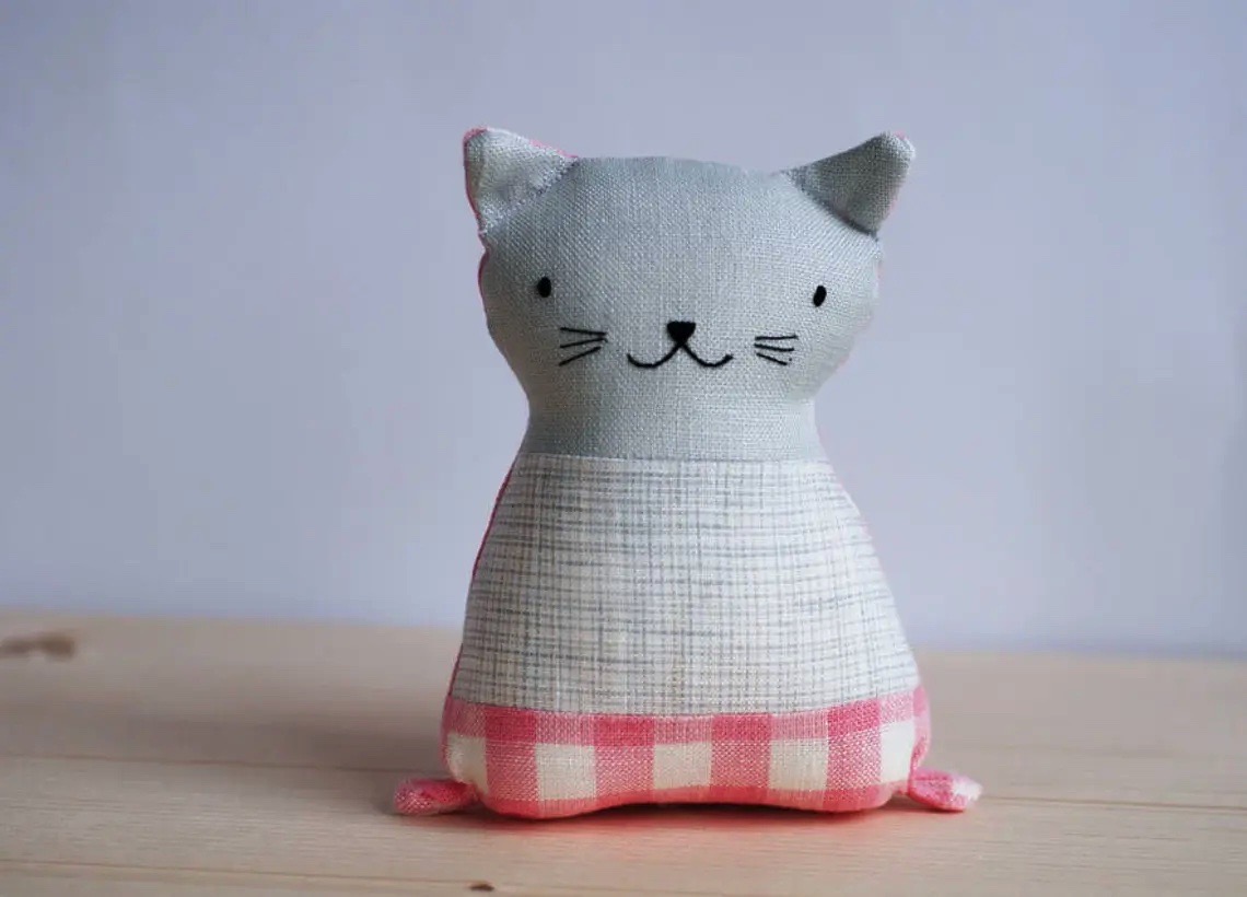 Boneco de tecido em forma de gato com padrões em bege e rosa