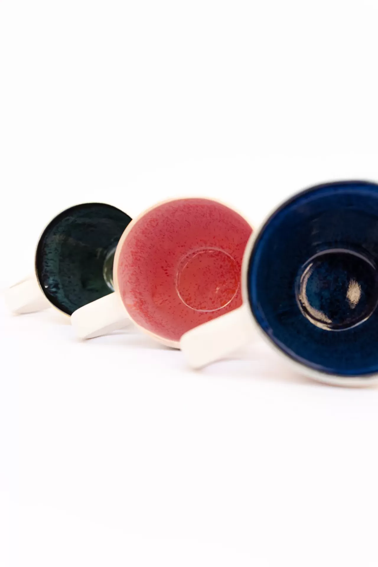 Três chávenas de café com interior colorido azul, vermelho e verde escuro e cabos brancos.