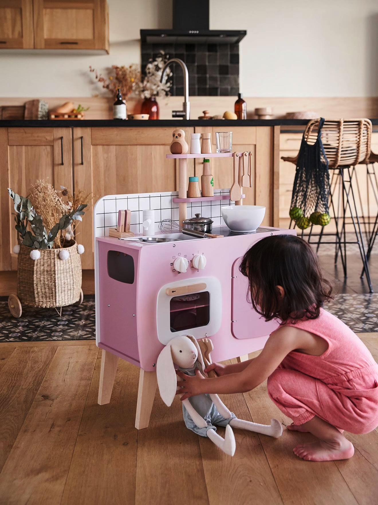 Brinquedo de cozinha cor-de-rosa com menina a brincar e cozinha real ao fundo