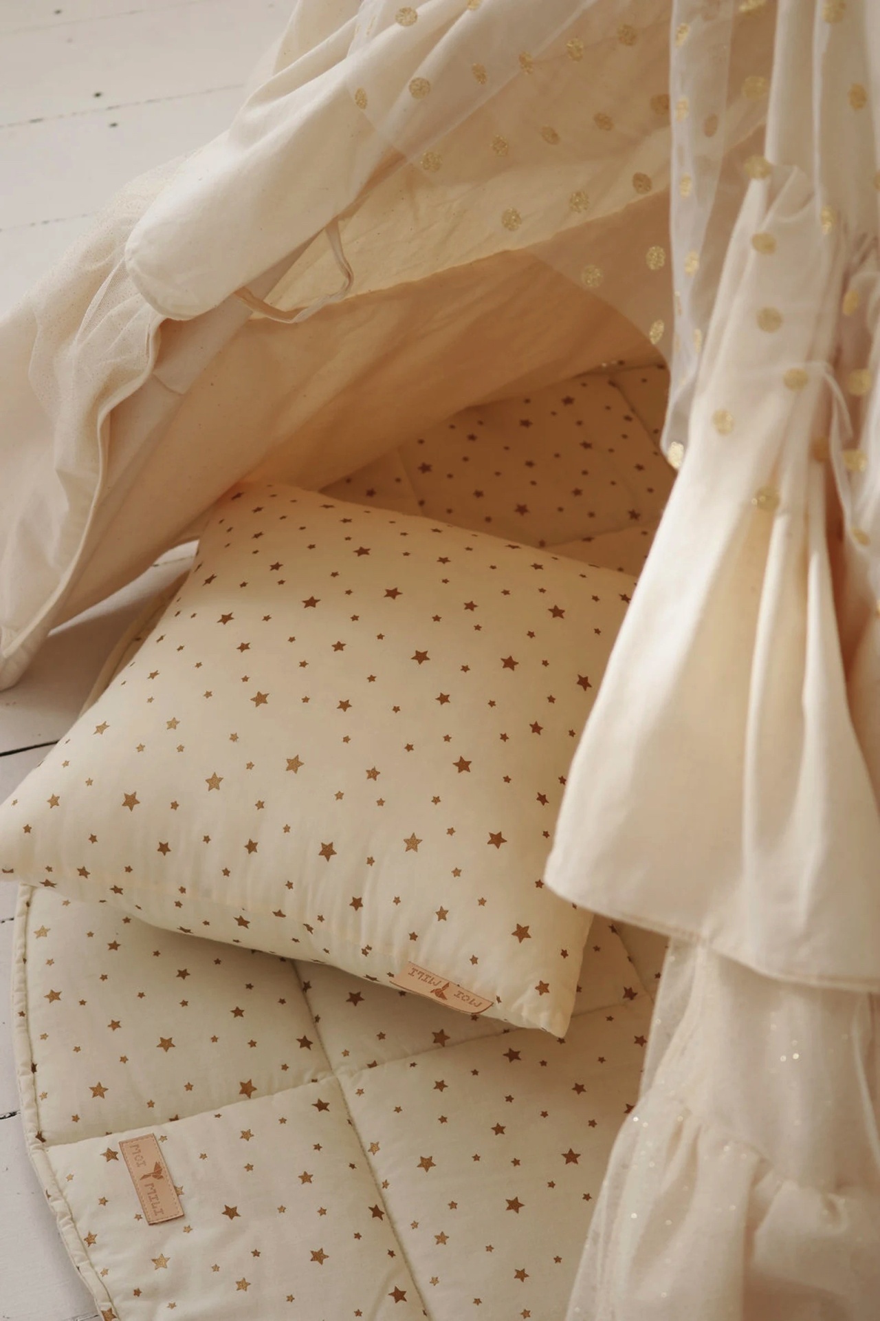 Almofada e colchão com estrelas douradas sob tenda branca com detalhes bordados