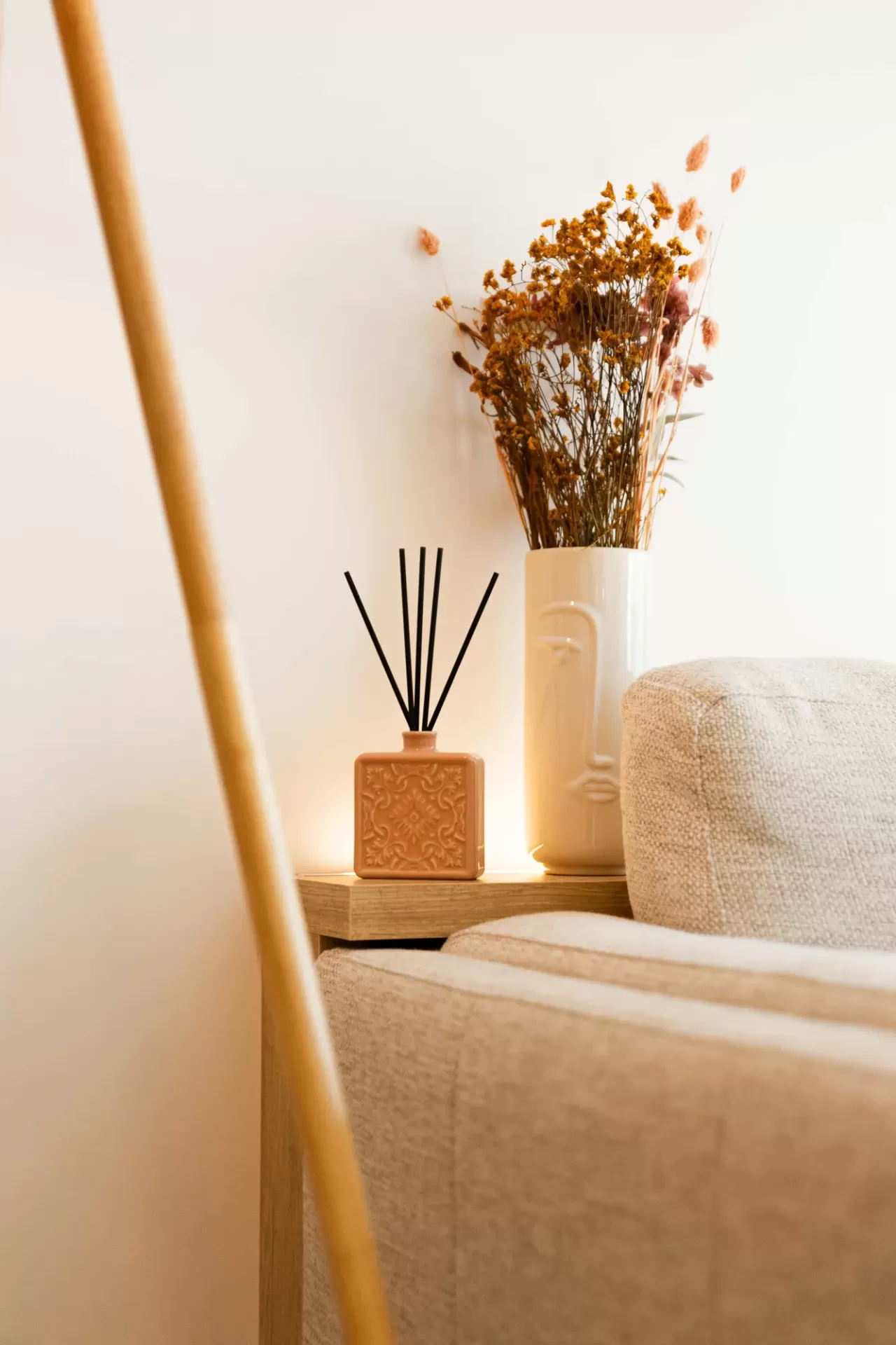Difusor de aroma rosa com flores secas em vaso branco ao lado de sofá bege