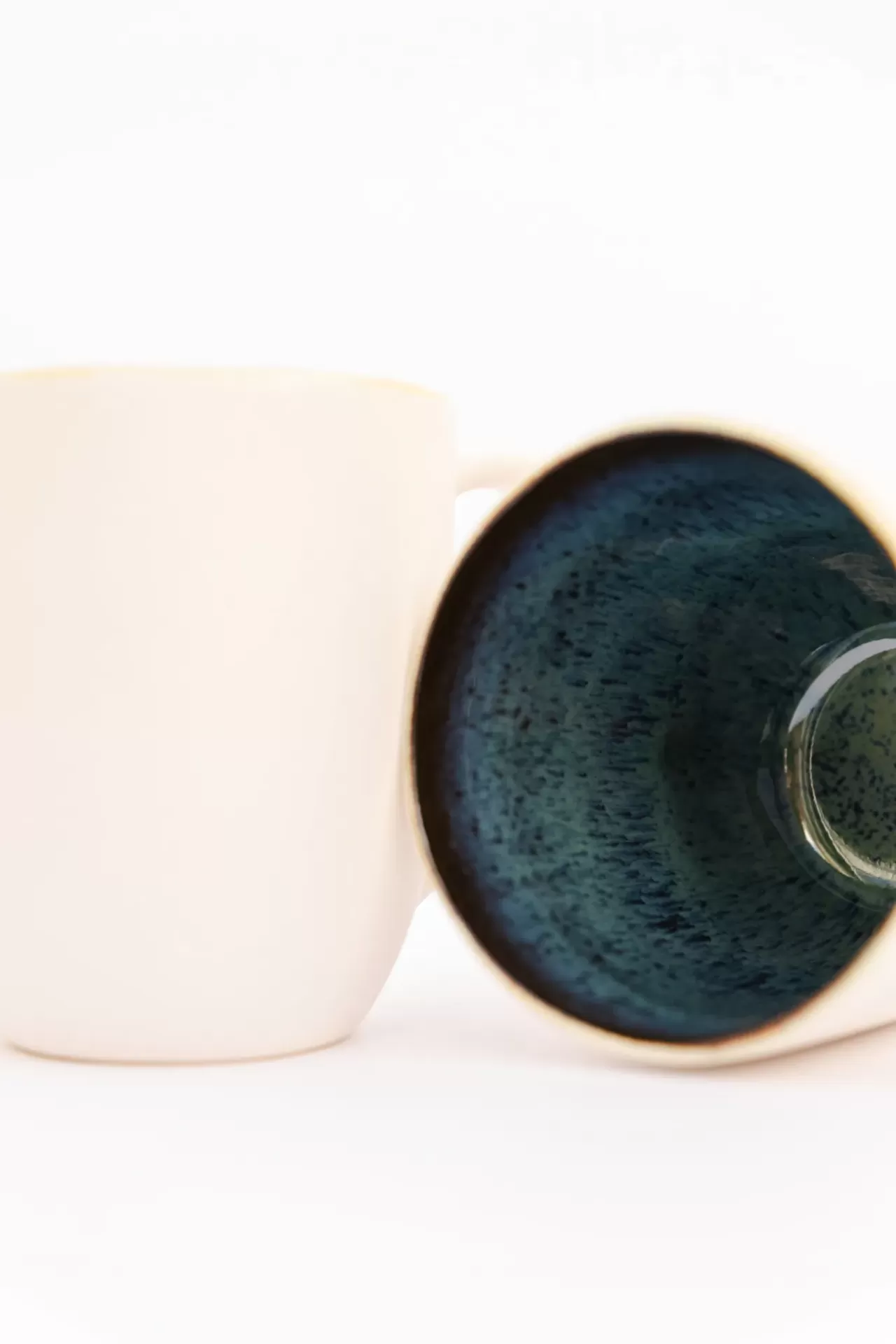 Duas canecas de cerâmica, uma bege e outra com interior azul texturado, sobre fundo branco.
