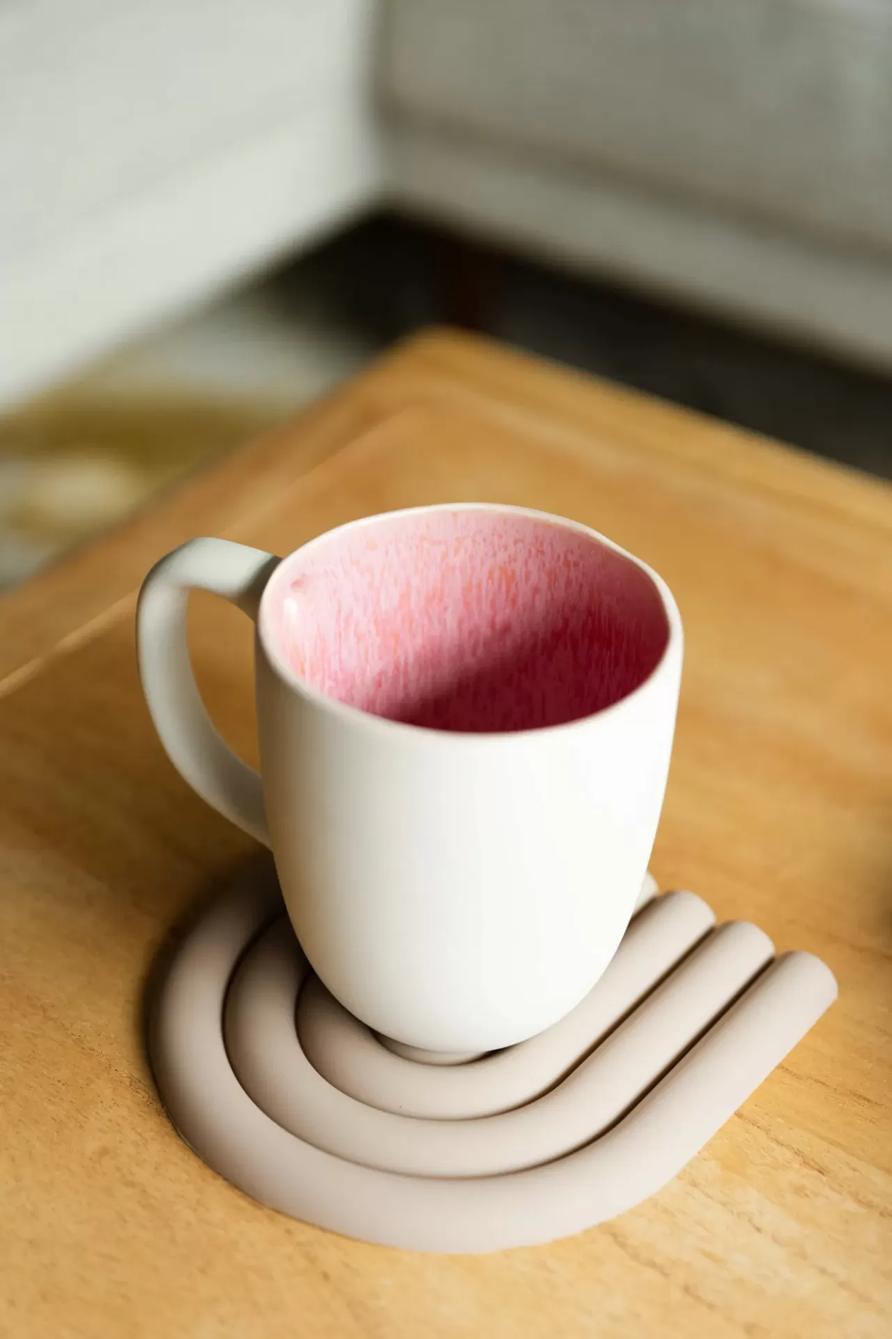 Caneca branca com interior rosa texturado sobre descanso cinza em mesa de madeira clara
