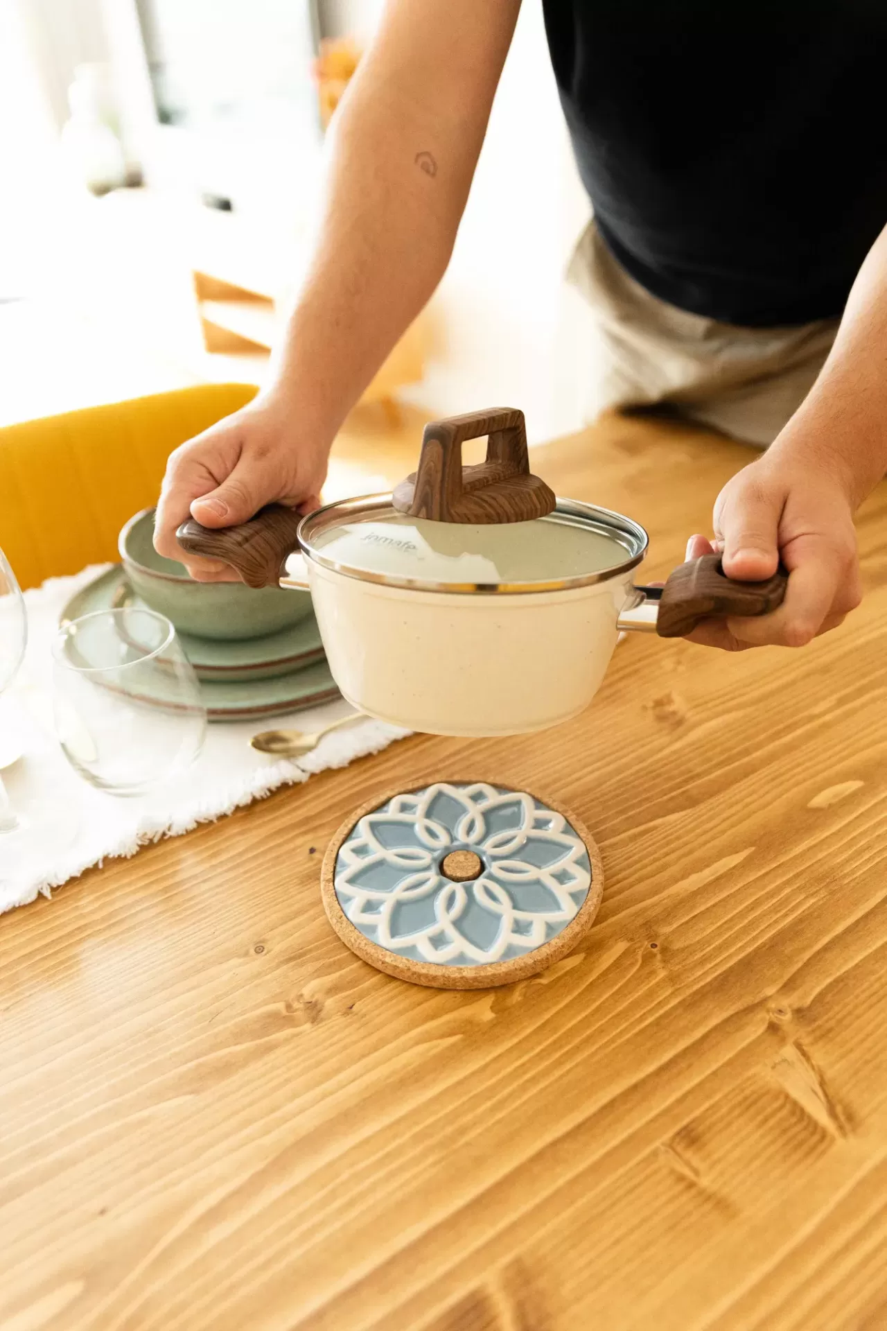 Panela creme com alças que parecem madeira sobre mesa de madeira com descanso de panela azul e cortiça.