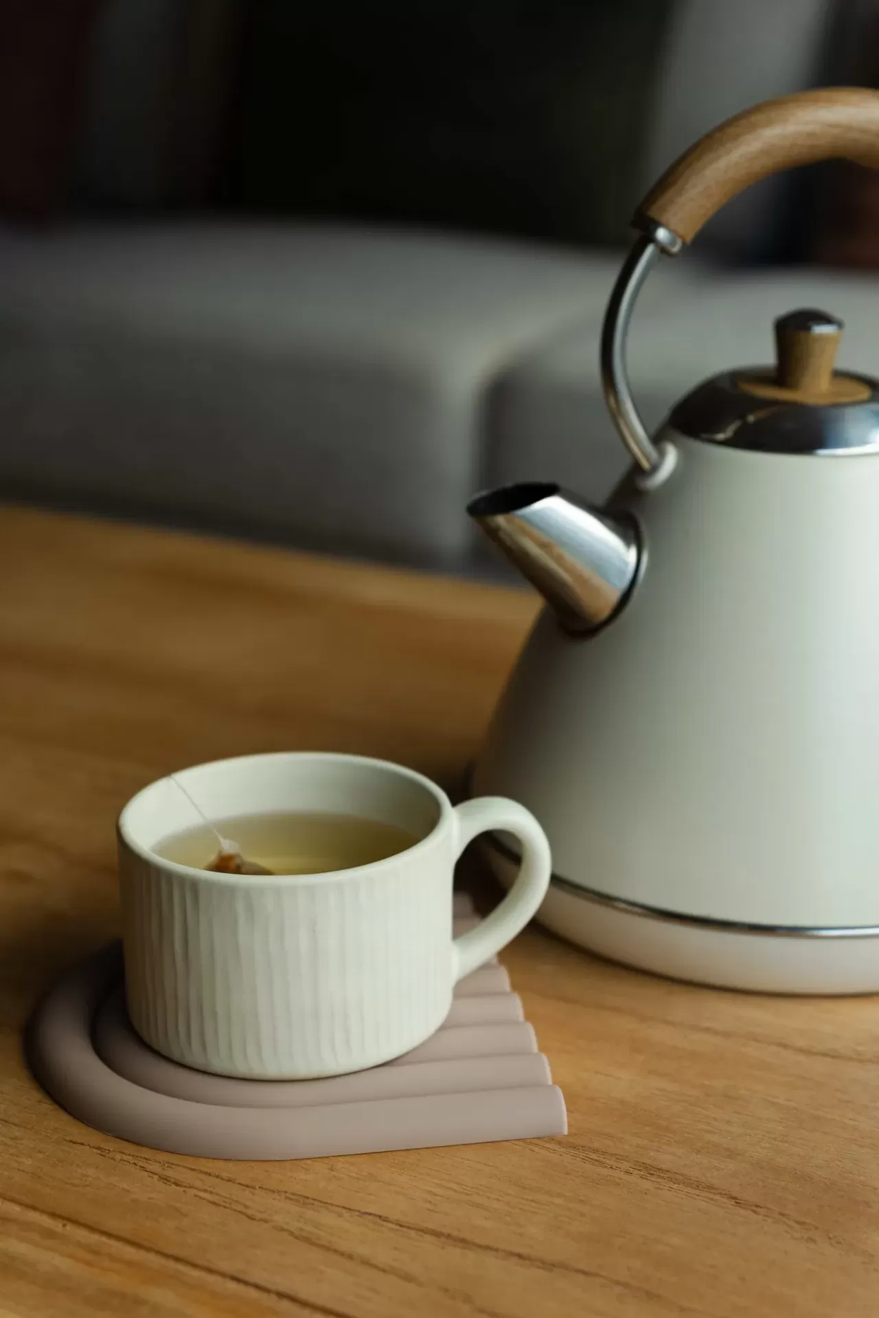 Bule de chá branco com cabo de madeira e chávena com chá em cima de mesa de madeira.