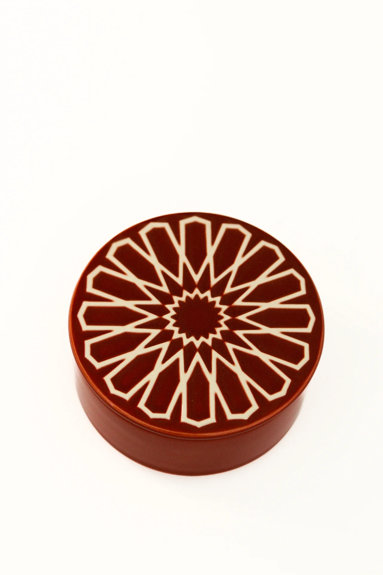 Caixa redonda castanha com padrão geométrico branco na tampa