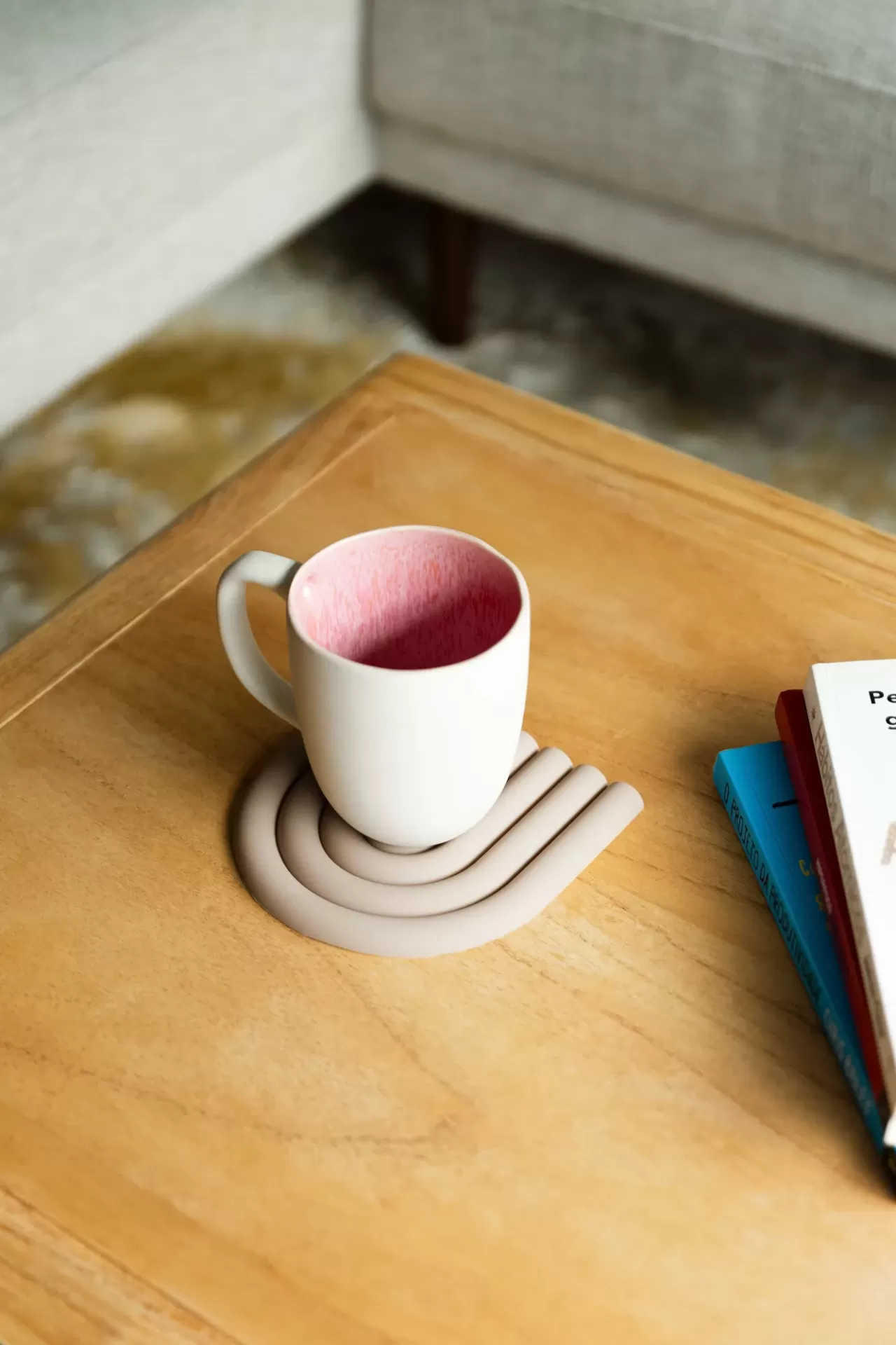 Xícara branca com interior rosa sobre descanso de copo cinzento numa mesa de madeira com livros ao lado