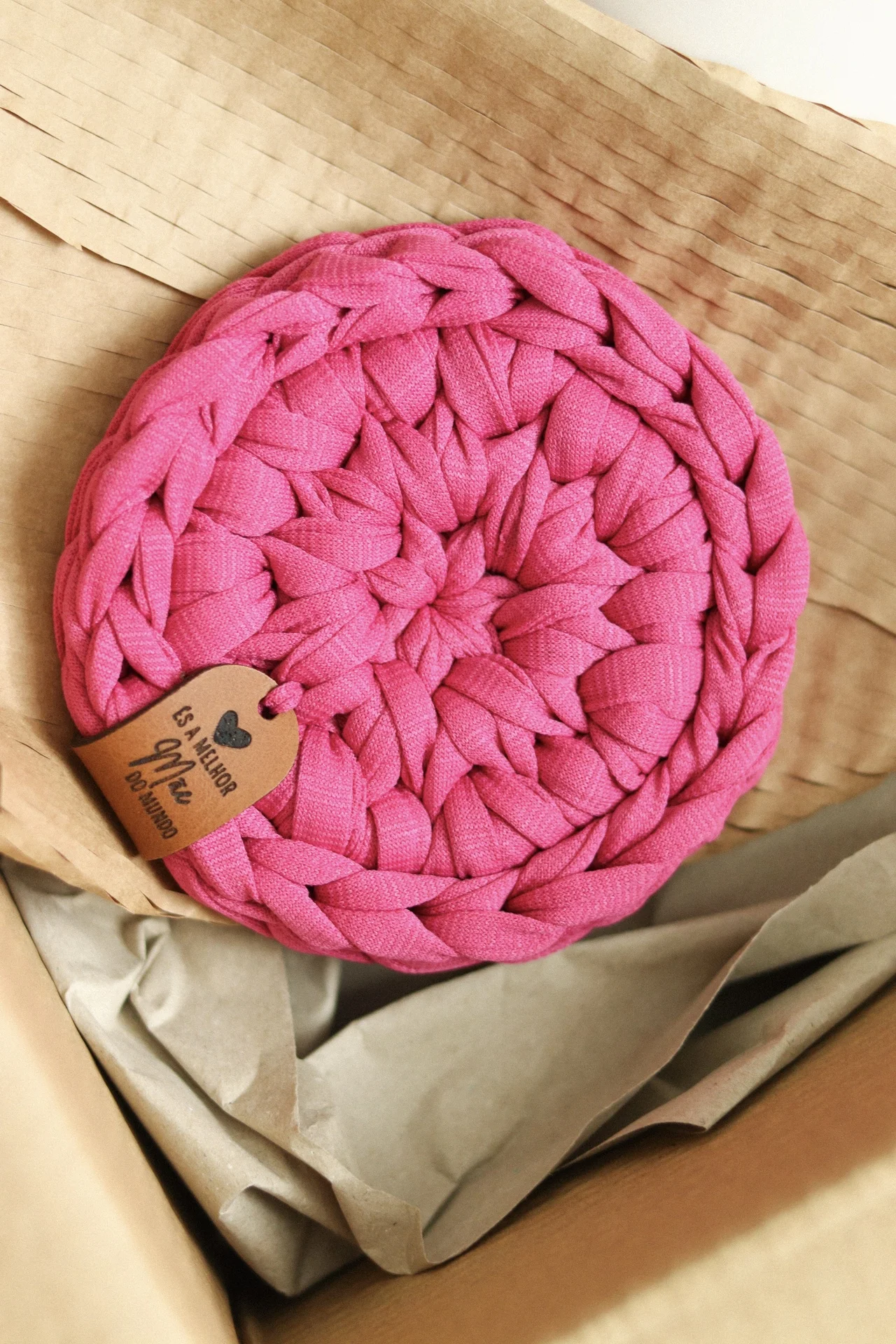 Cesto redondo de tecido cor-de-rosa trançado com etiqueta e embalagem de papel castanho em caixa.