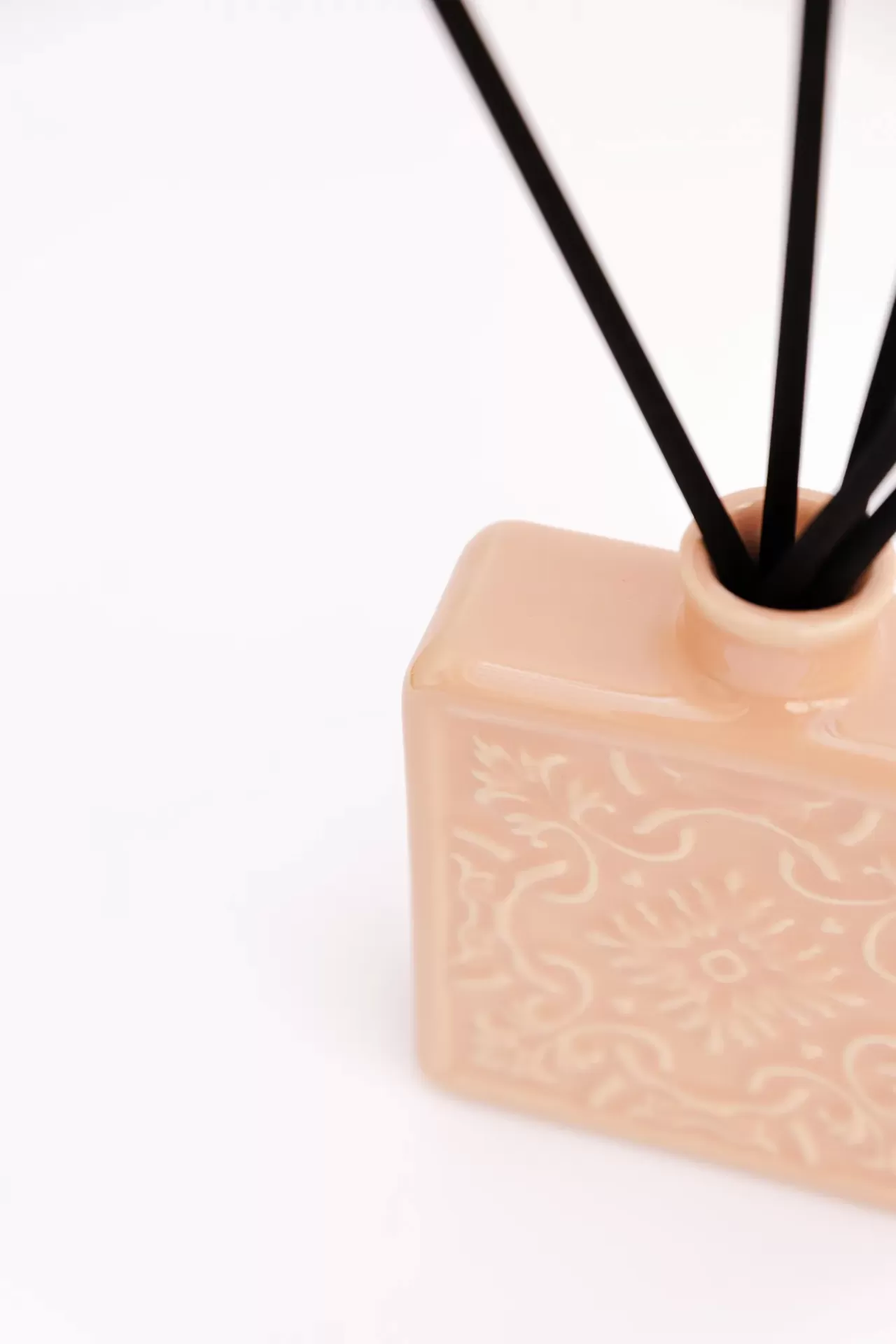 Difusor de aromas em cerâmica cor de rosa com varas pretas num fundo branco