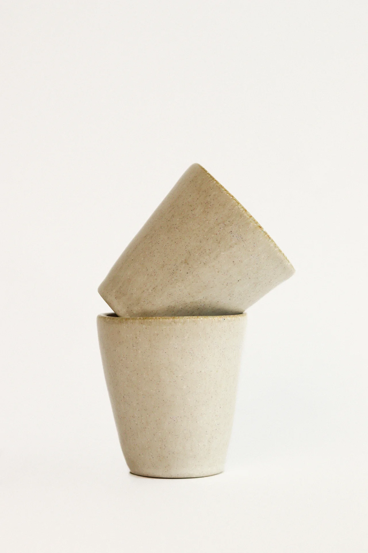 Dois copos empilhados em cerâmica bege com fundo branco