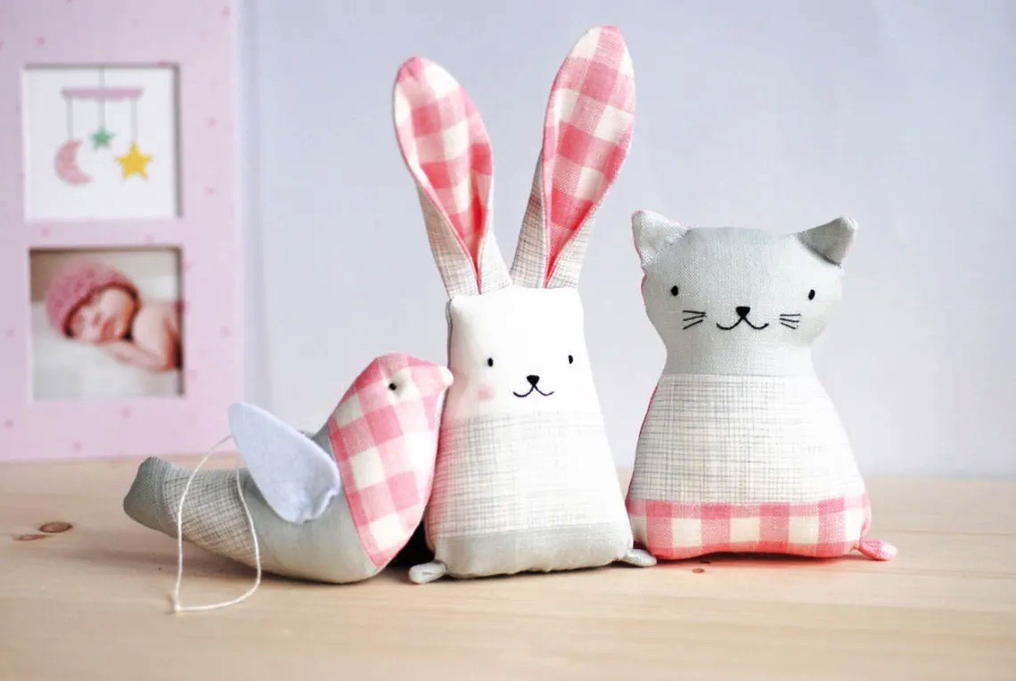 Três brinquedos de tecido em forma de animal sobre uma mesa de madeira clara.