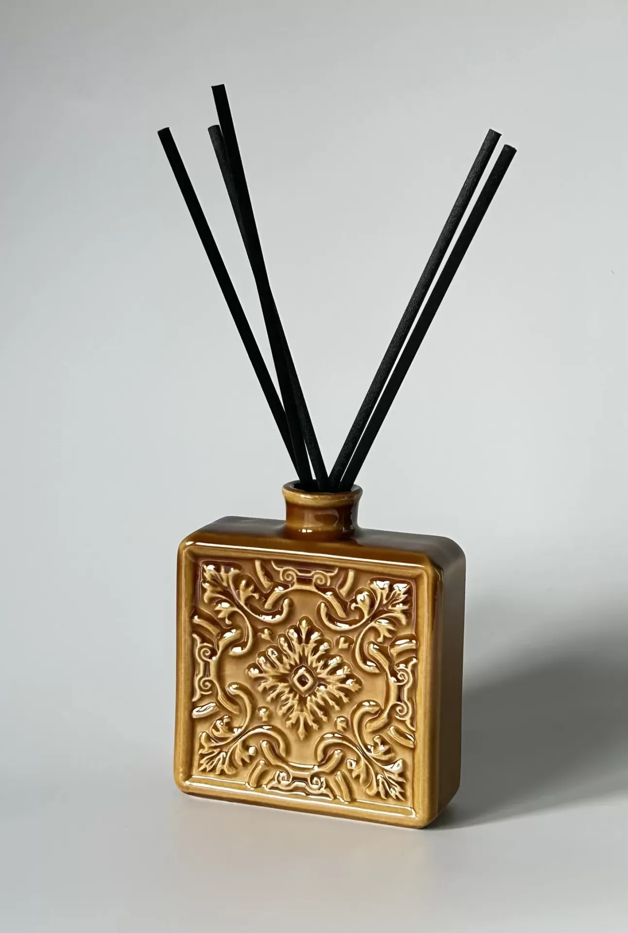 Frasco cerâmico castanho com decoração em relevo e varetas pretas de difusor de aroma.