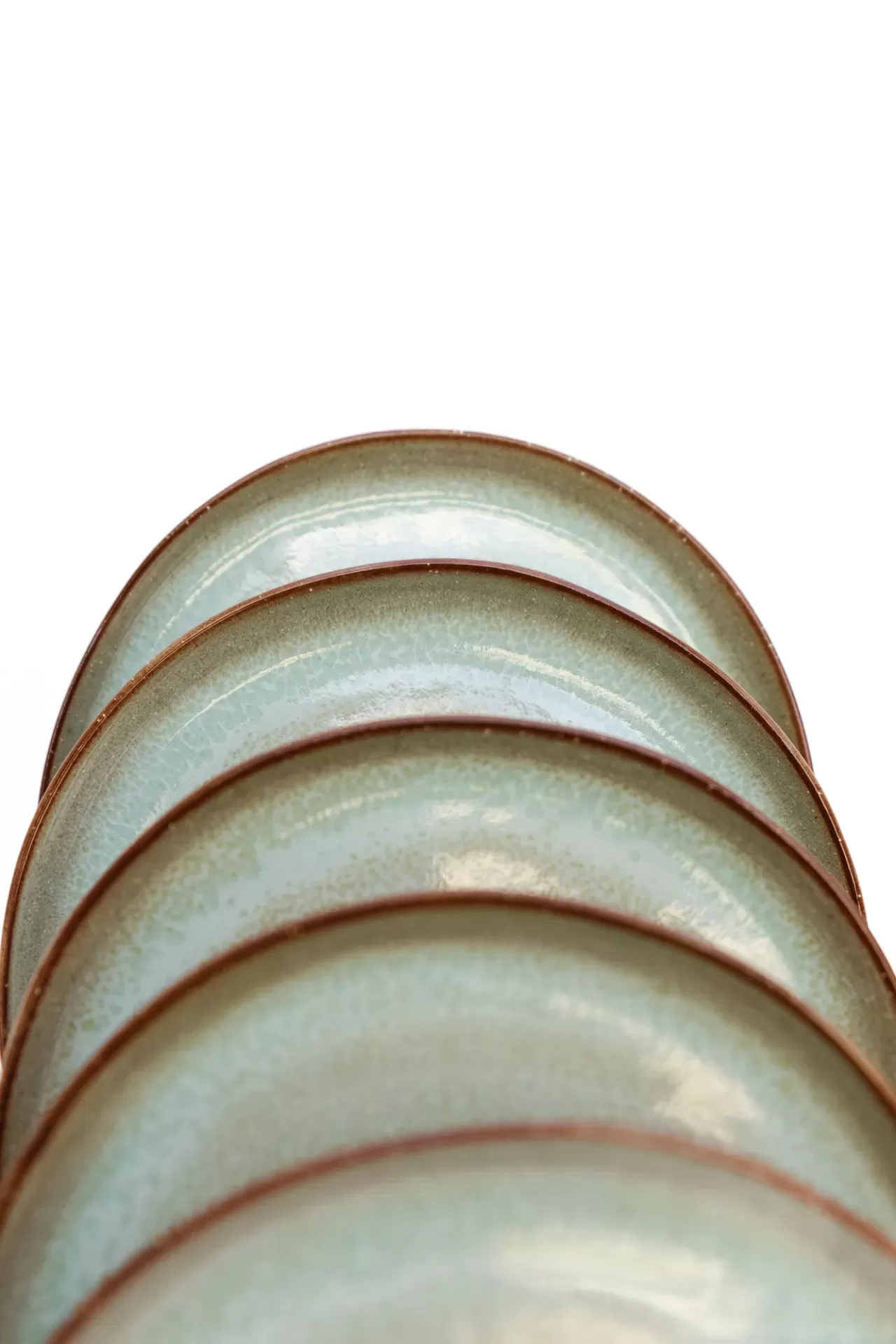 Cinco pratos redondos em cerâmica azul esverdeada com bordas castanhas empilhados.