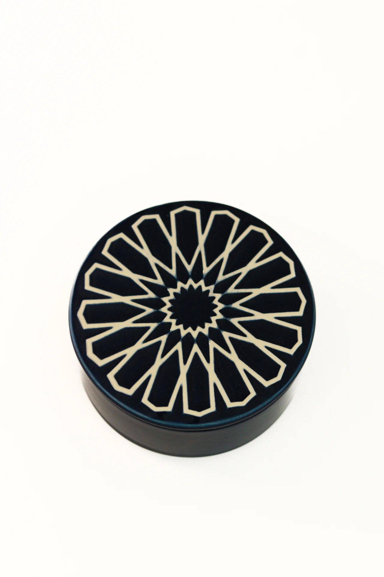 Caixa redonda preta com padrão geométrico creme na tampa