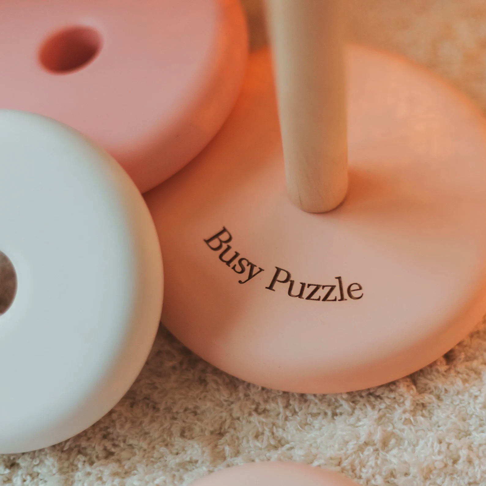Peças redondas de madeira em tons pastel como parte de um brinquedo empilhável com inscrição Busy Puzzle