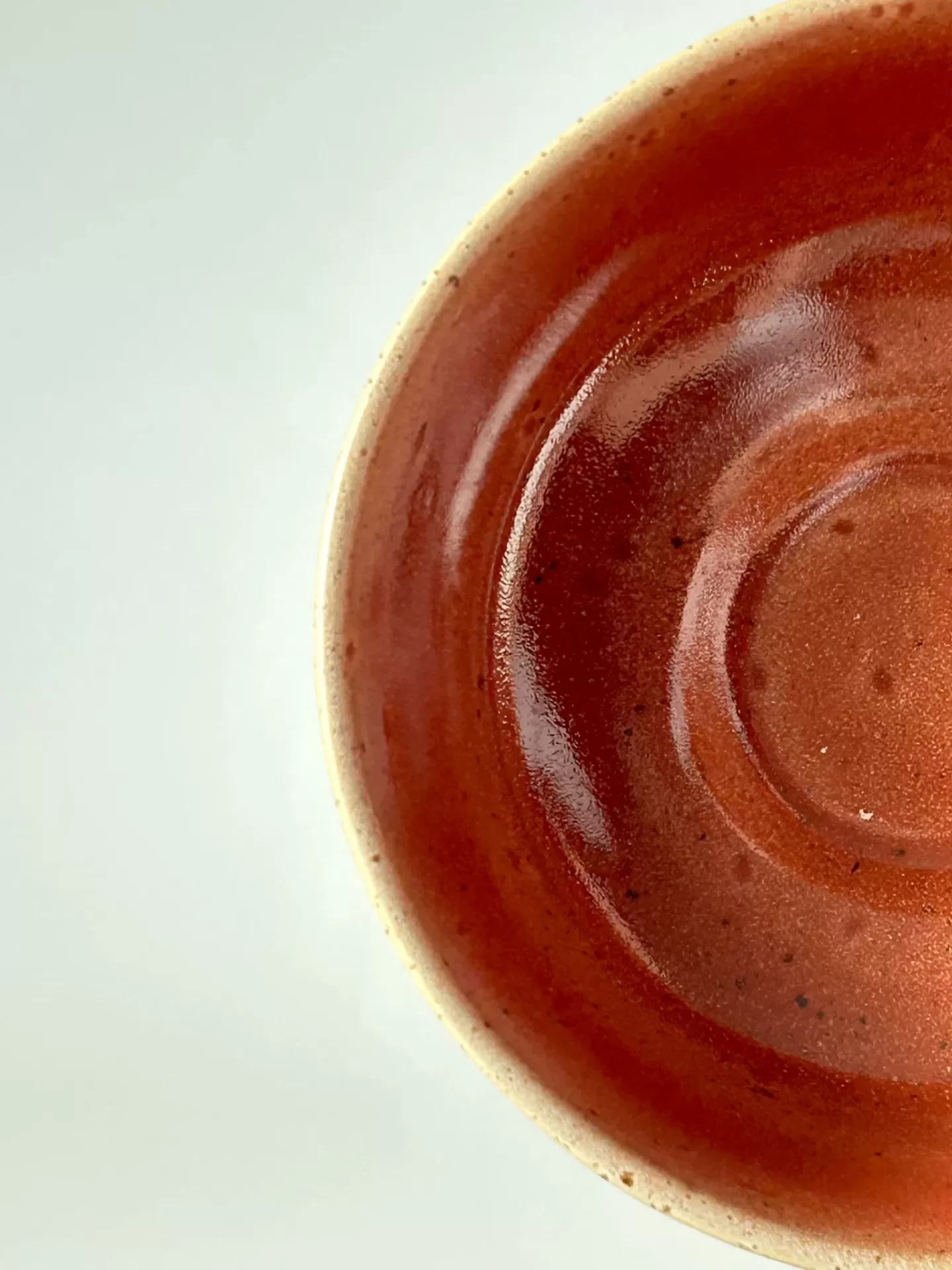 Parte de um prato de cerâmica vermelho e castanho brilhante sobre fundo branco