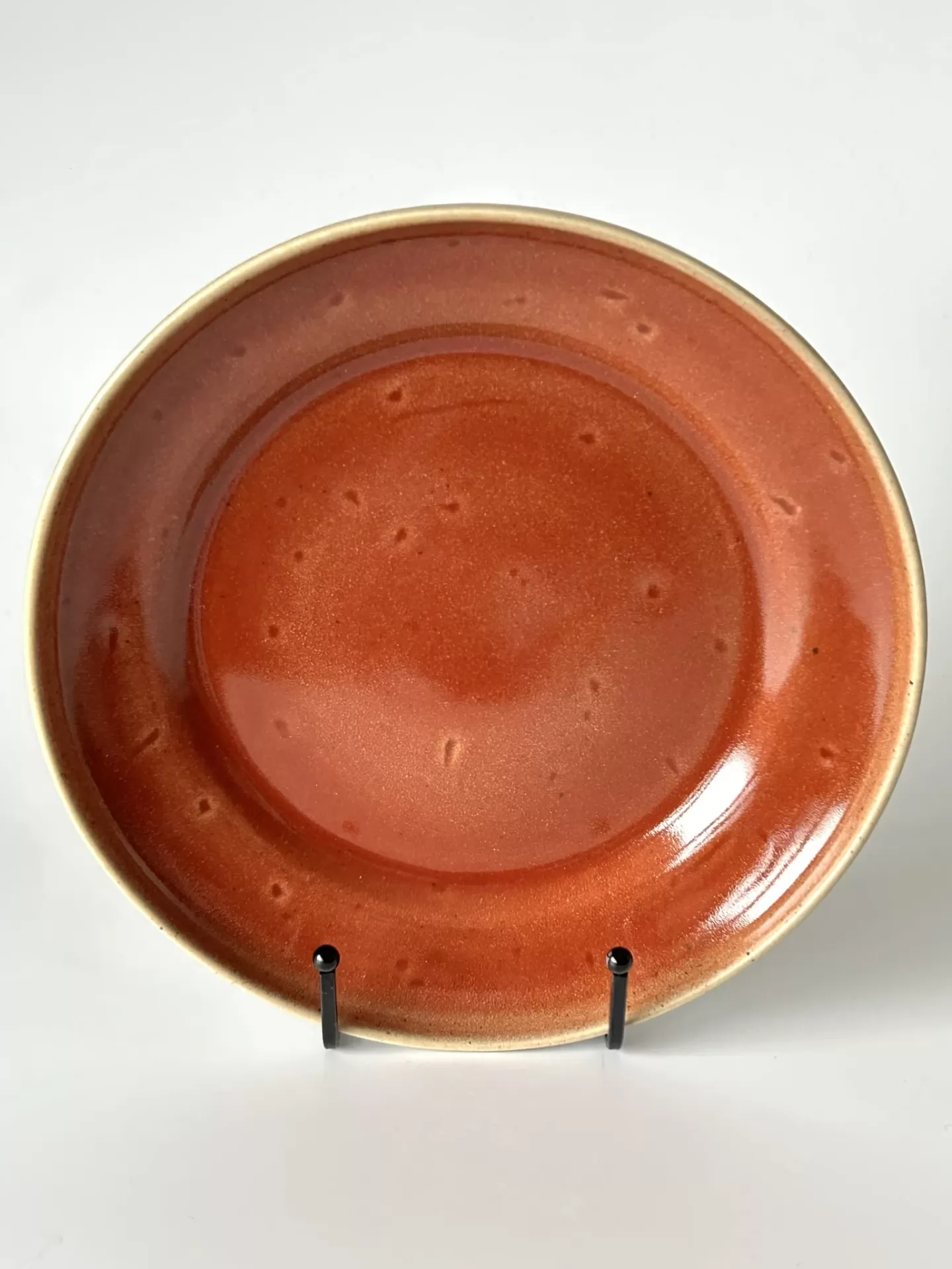 Prato redondo em cerâmica com borda bege e interior vermelho com textura e manchas.
