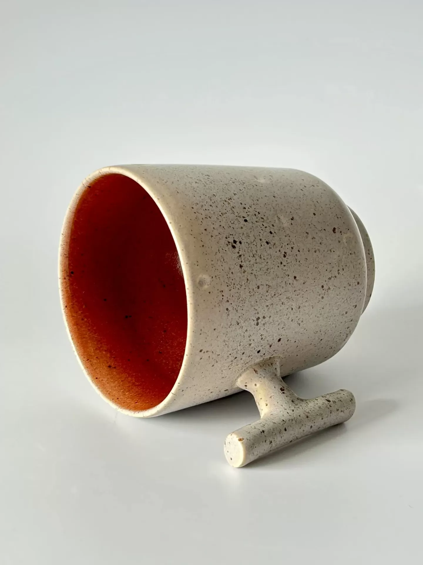 Caneca de cerâmica bege com interior vermelho alaranjado deitada sobre fundo branco