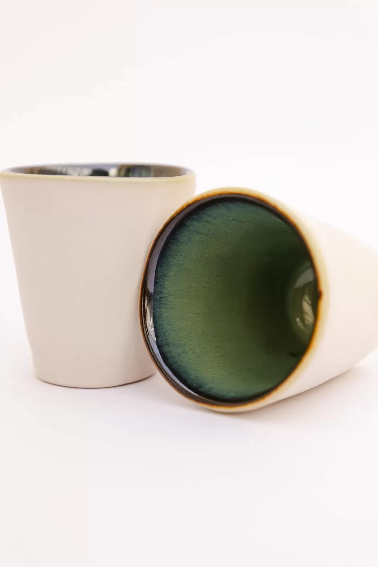 Dois copos de cerâmica em fundo branco, um com interior verde e exterior bege.