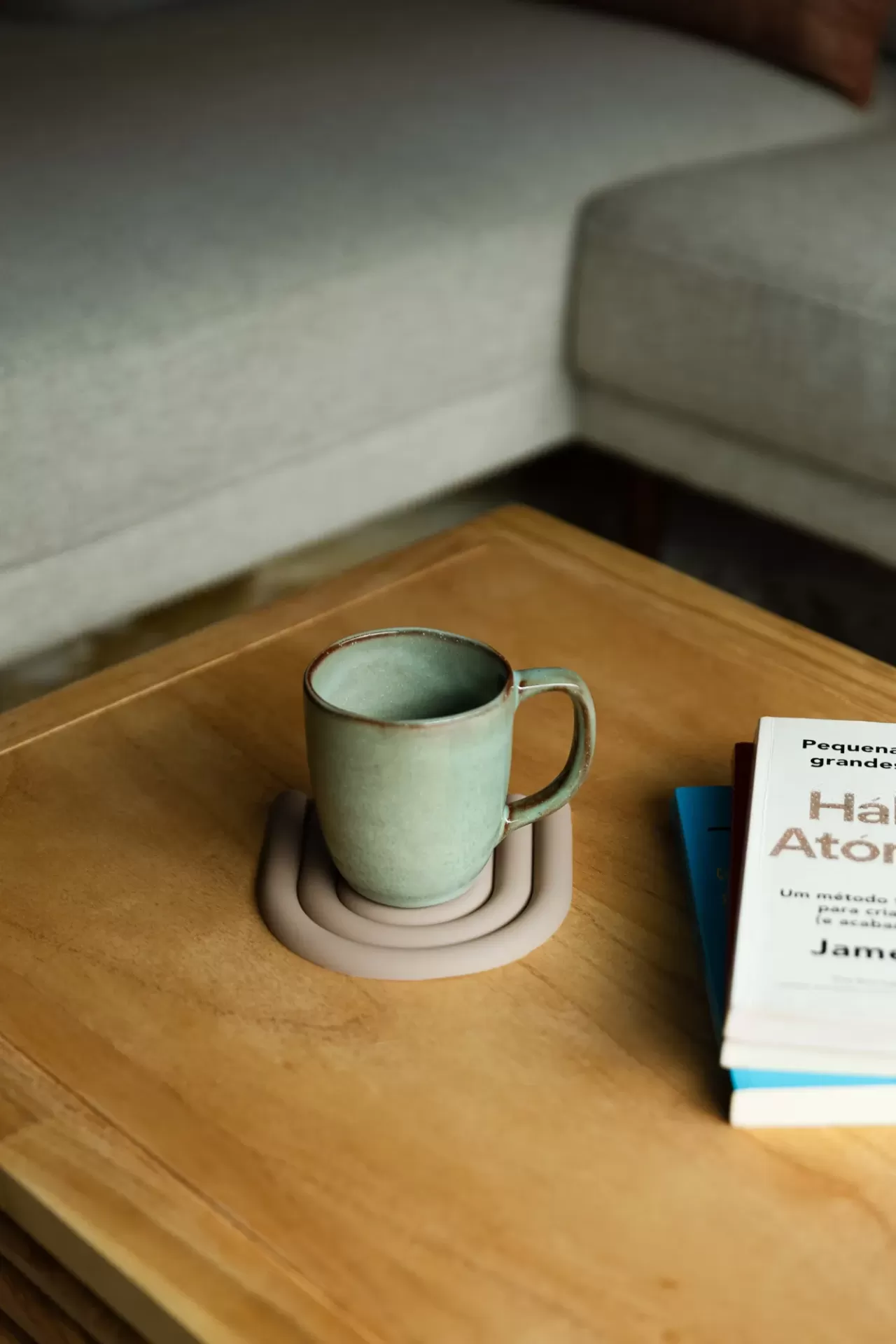 Caneca verde de cerâmica sobre suporte castanho claro numa mesa de madeira com livros ao lado