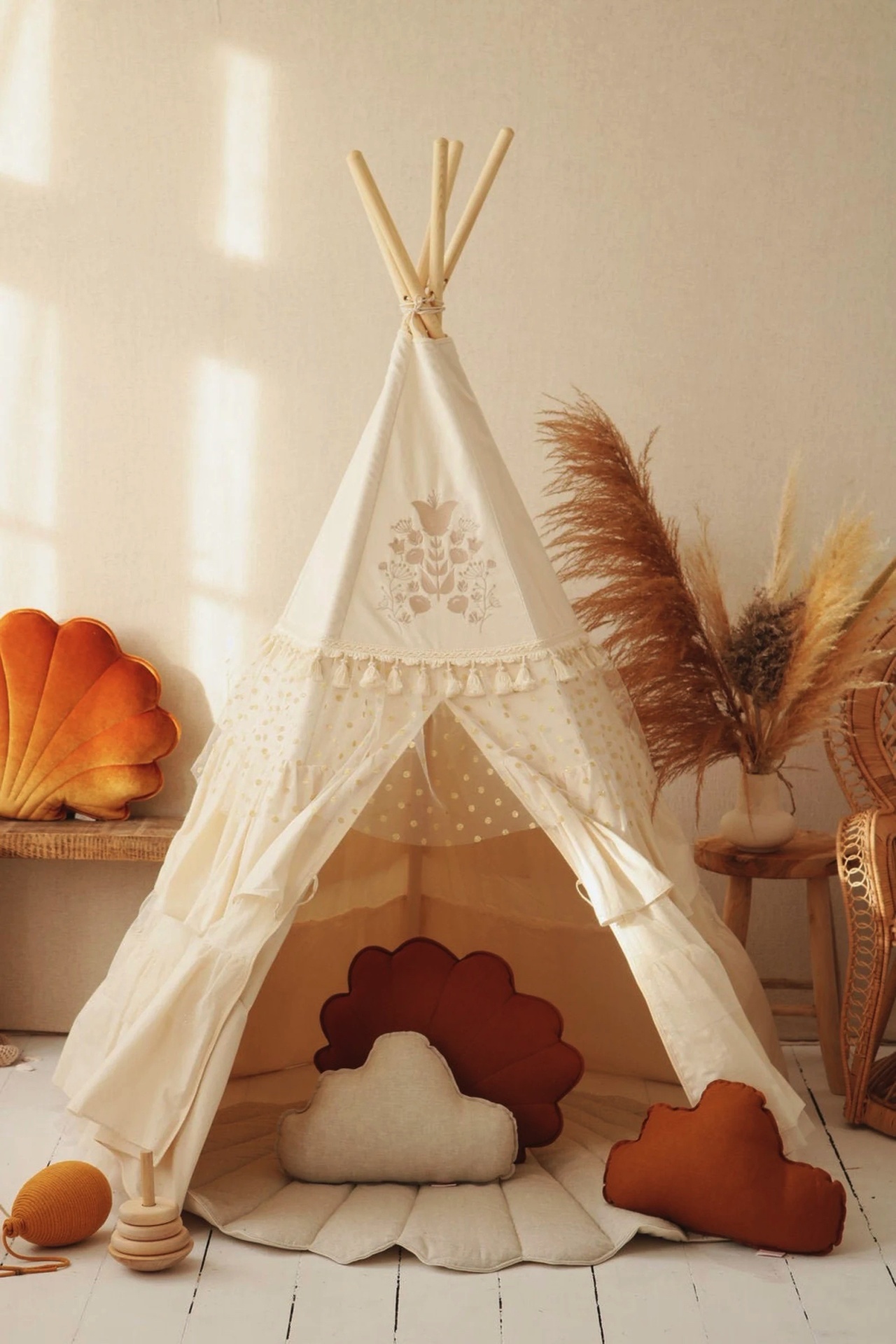 Tenda tipi branca com almofadas de nuvem tons terra e tapete bege num espaço claro e natural.