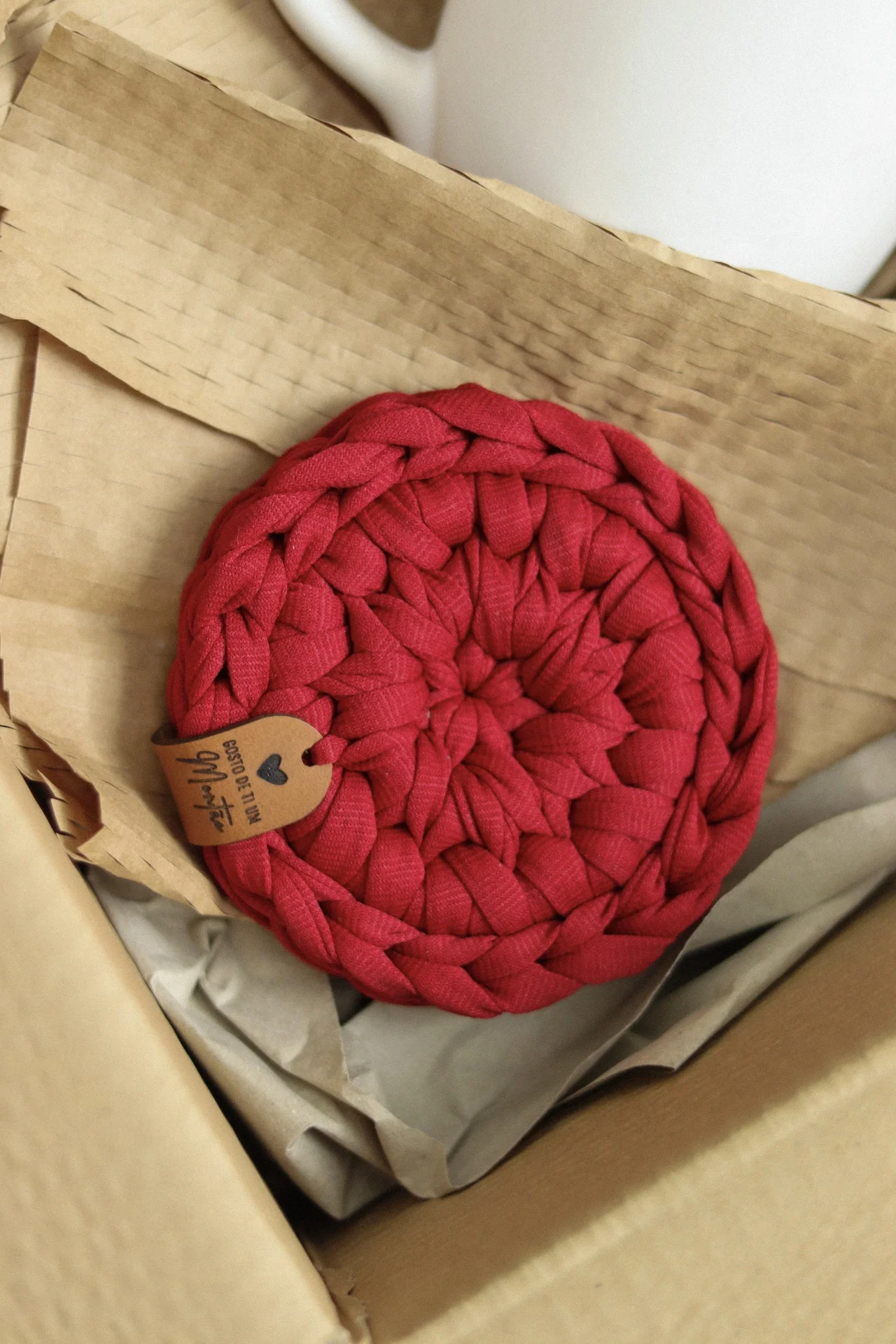 Tapete vermelho trançado em caixa de cartão com etiqueta de couro