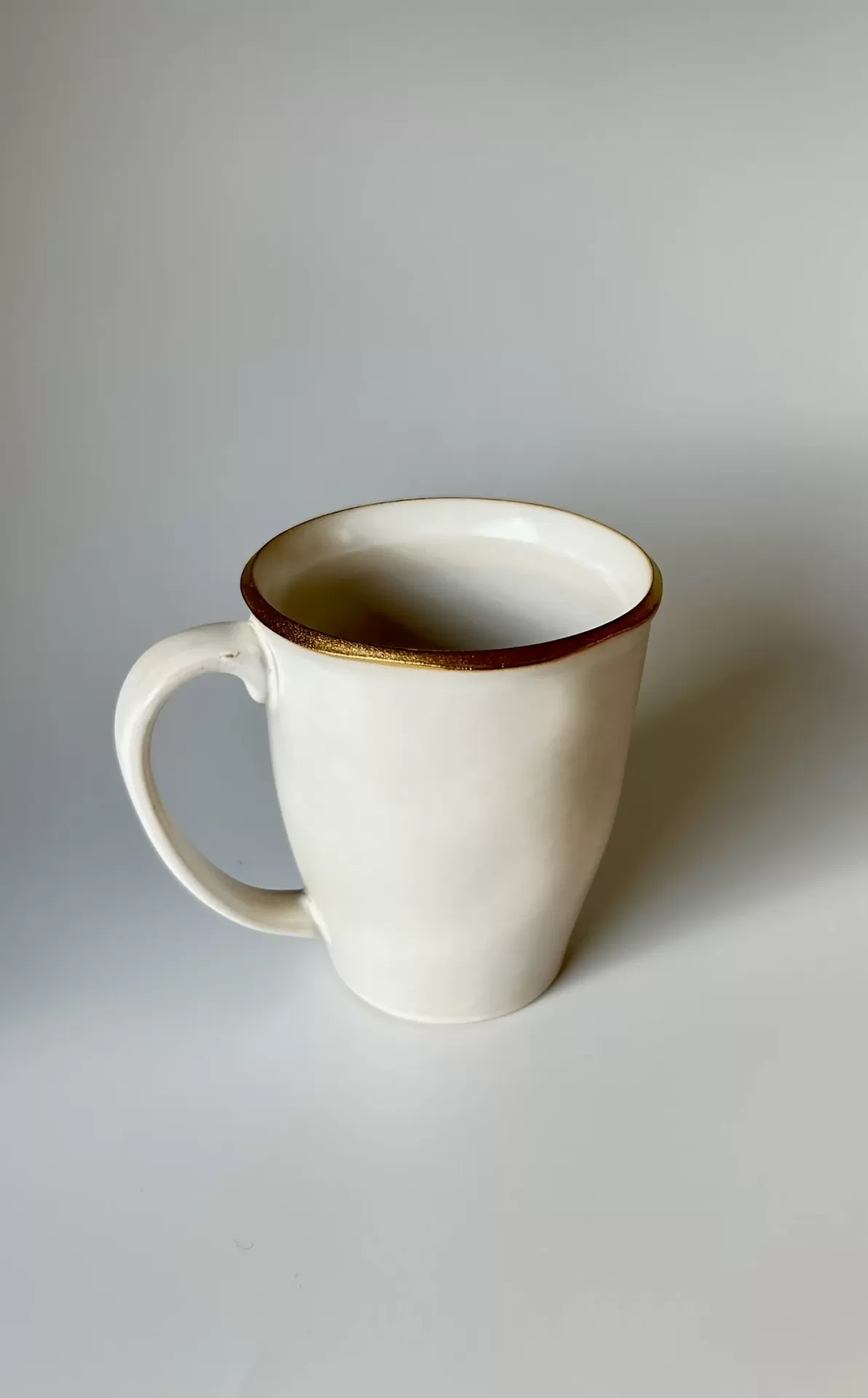 Caneca branca com bordo dourado em fundo cinzento.