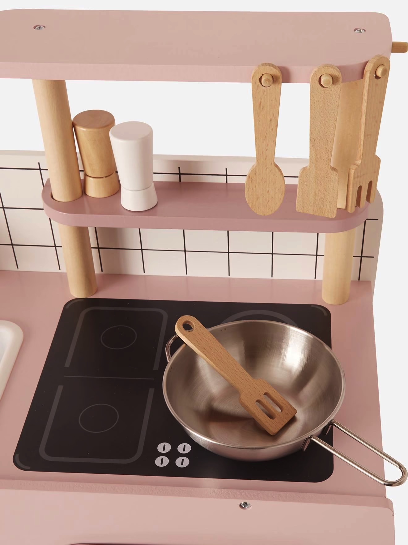 Cozinha infantil de brinquedo rosa com panela metálica e utensílios de madeira.
