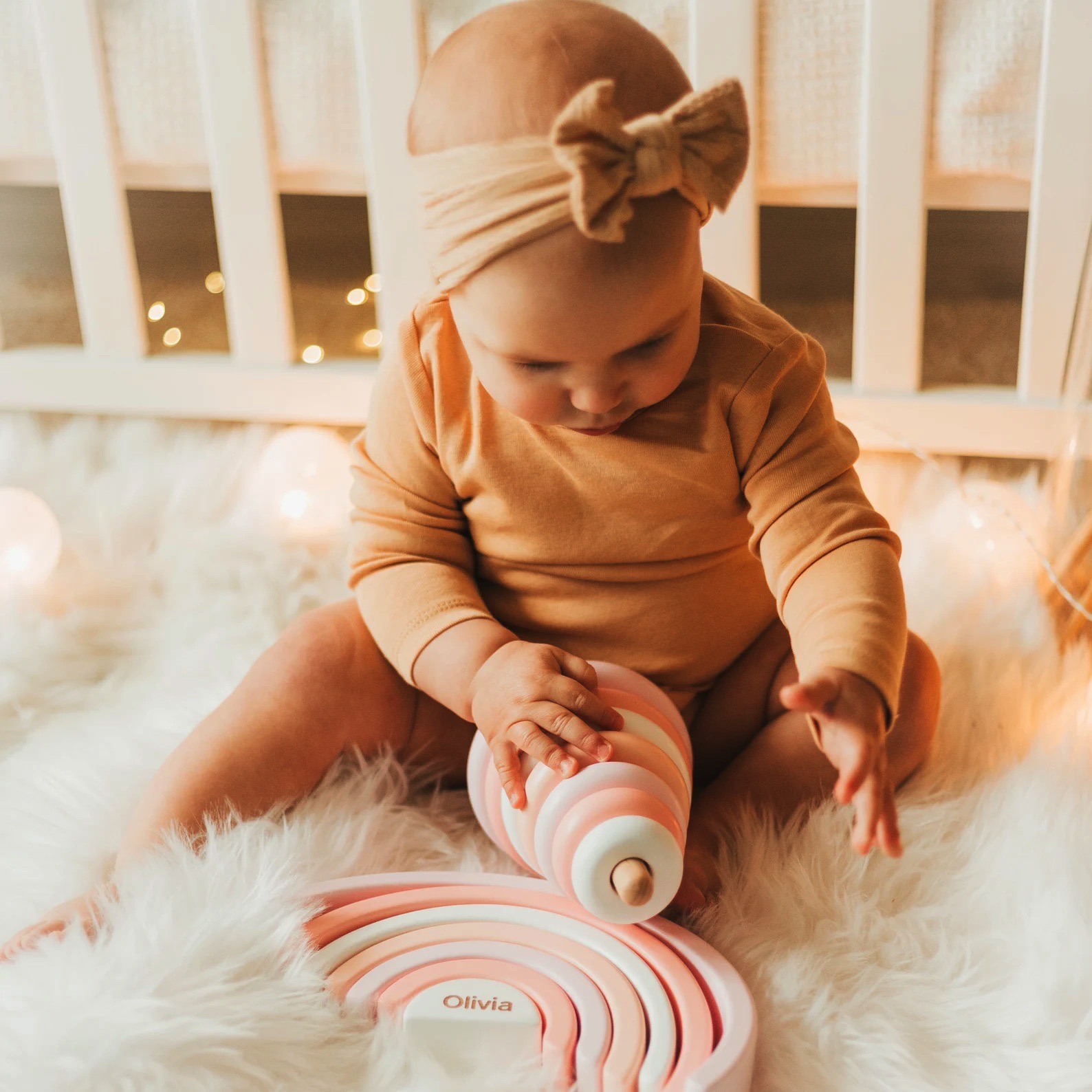 Bebé a brincar com brinquedo de madeira em forma de arco-íris rosa e branco