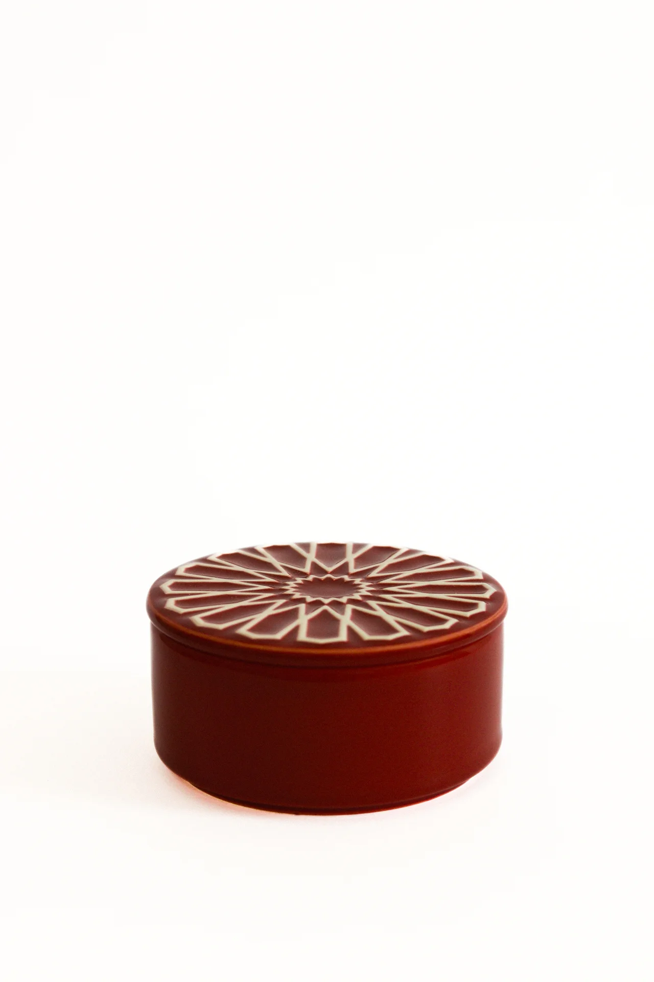 Caixa redonda vermelha com tampa decorada em padrão geométrico branco