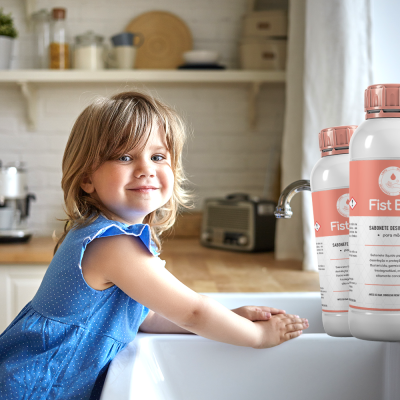 Três frascos de produto Fist Bac rosa e branco sobre bancada de cozinha com criança de vestido azul