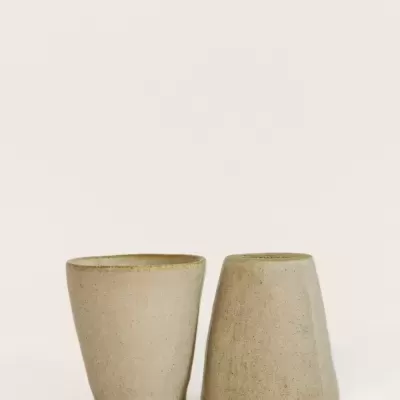Dois copos de cerâmica bege com textura rugosa em fundo branco.