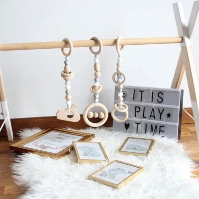 Estrutura de madeira para brinquedos de bebé com três brinquedos pendurados, quadro com texto IT IS PLAY TIME e quatro molduras no chão