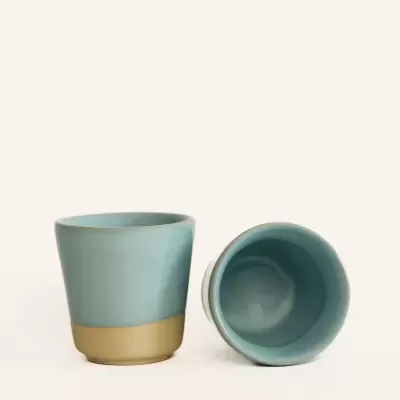 Dois copos de cerâmica azul celeste com base bege, um em pé e outro deitado